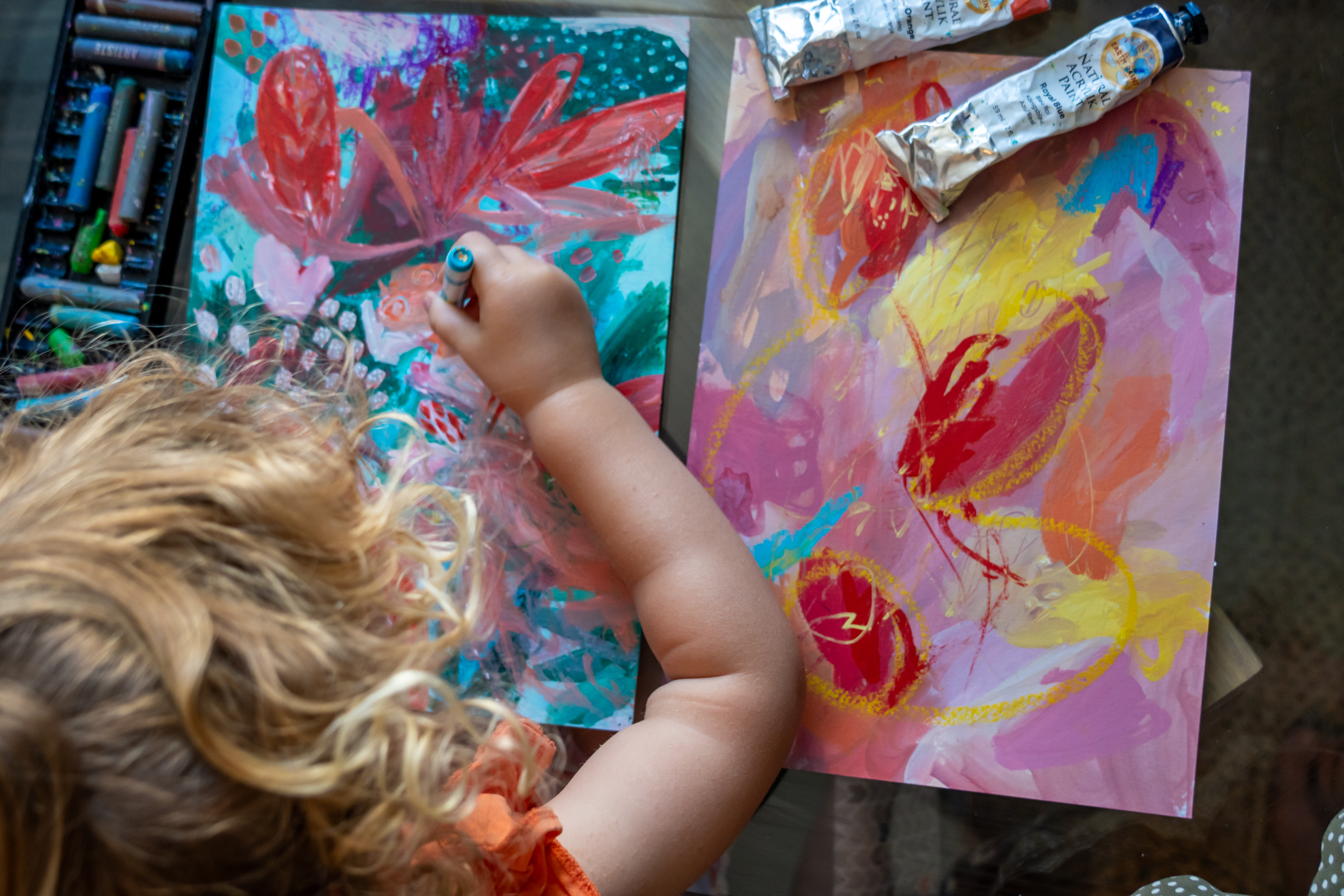 A child painting alongside colourful abstract pieces and natural paints